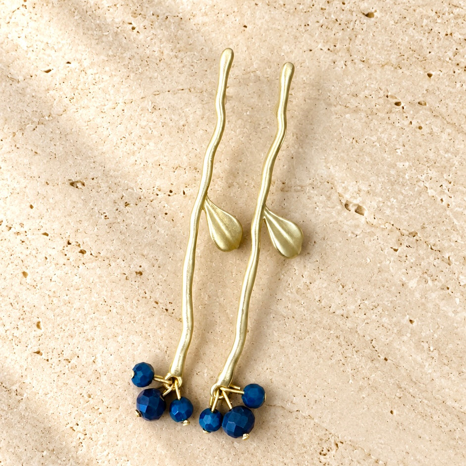 Pendientes Rama Endrina largos con ramas doradas y pequeños cristales azules, sobre fondo claro.